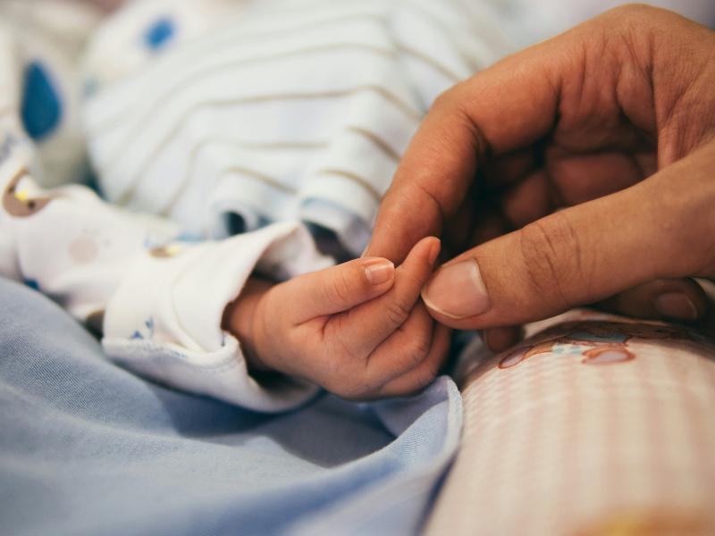 Eine große Hand einer erwachsenen Person hält eine kleine eines Babys.